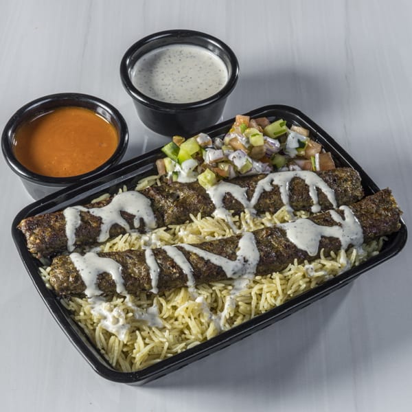Halal lamb kofta kebabs over rice with white sauce, salsa, and a side of red sauce.