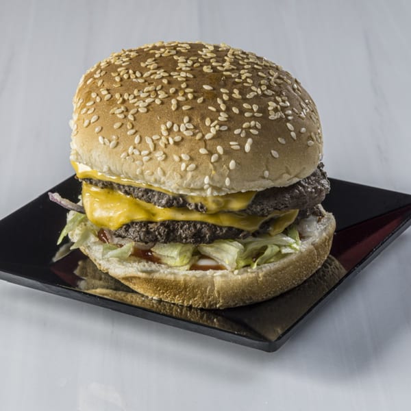 Double cheeseburger with sesame seed bun, lettuce, and sauce on a black square plate.
